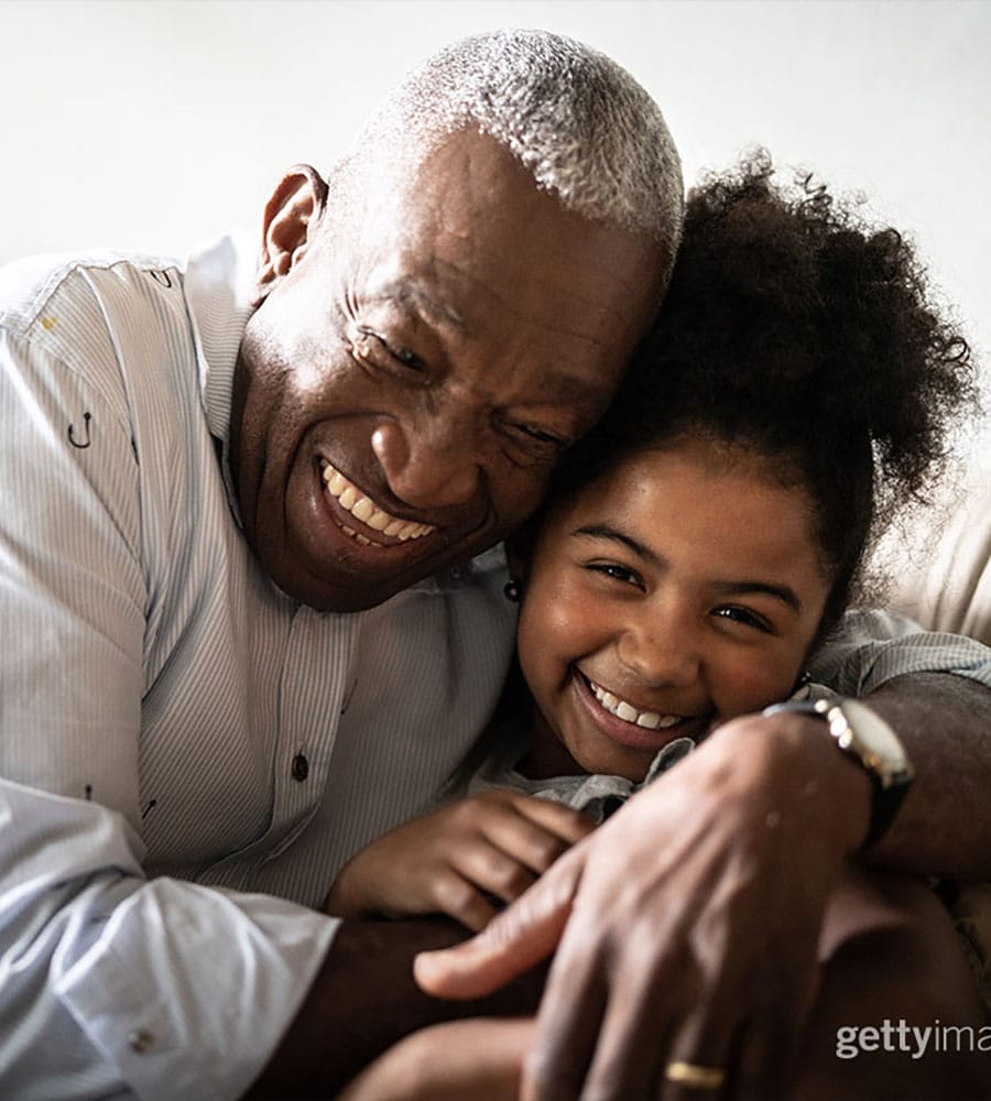 A joyful grandfather embracing his granddaughter, both smiling and sharing a warm, affectionate moment together.