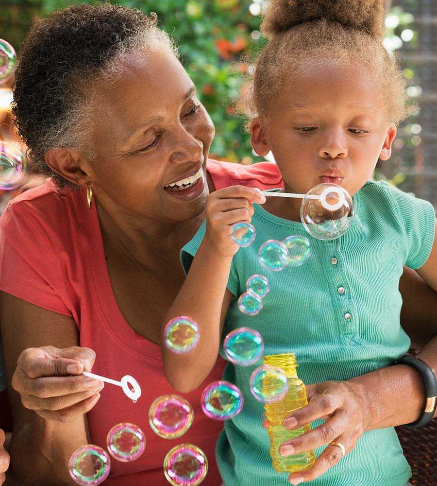 A joyful grandmother with her grandchild, blowing soap bubbles in a sunny garden setting.