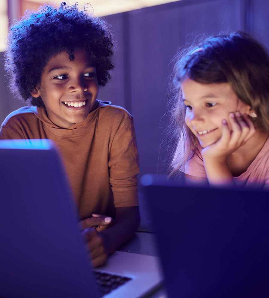 Two elementary school students smiling and using laptops, representing early AI awareness in education and media.