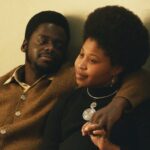 A Black man and woman share a tender moment in a still from the film Judas and the Black Messiah. The man embraces the woman as they look forward contemplatively.