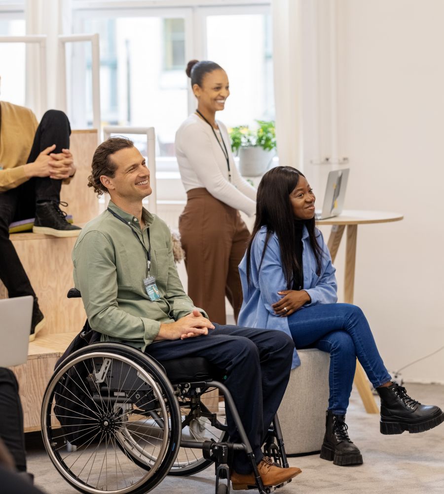 White man in wheelchair sitting amongst coworkers at a work presentation