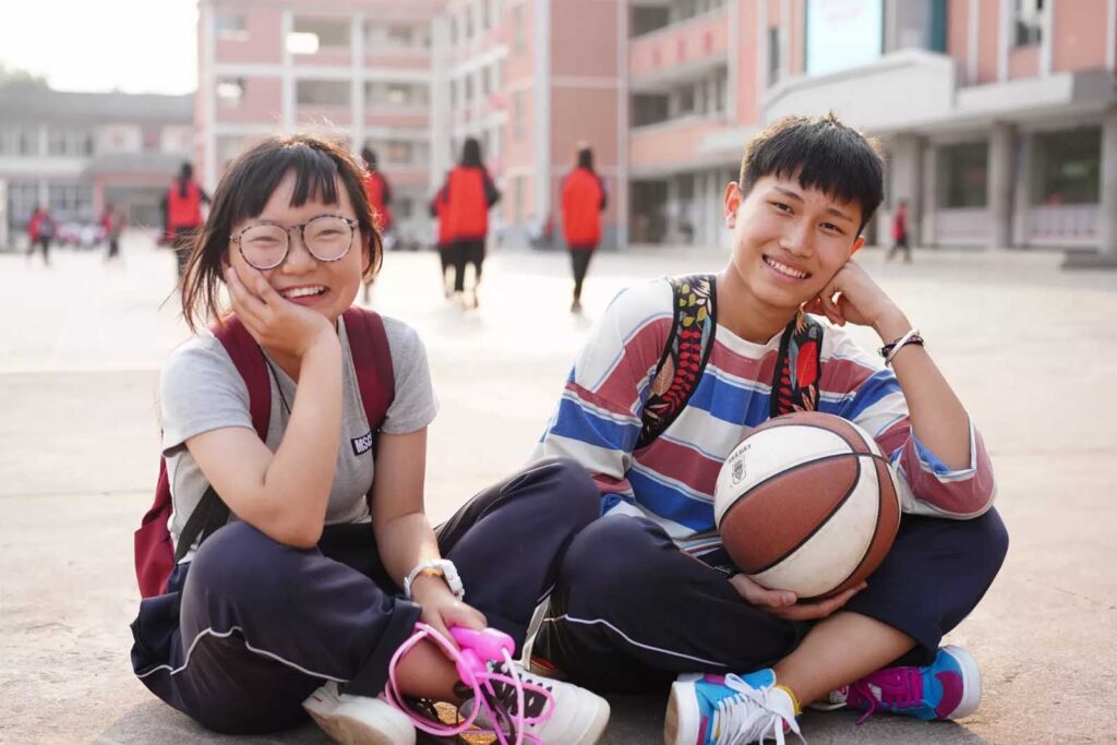 Smiling Chinese girl and boy sitting on school grounds, representing gender diversity in Chinese advertising