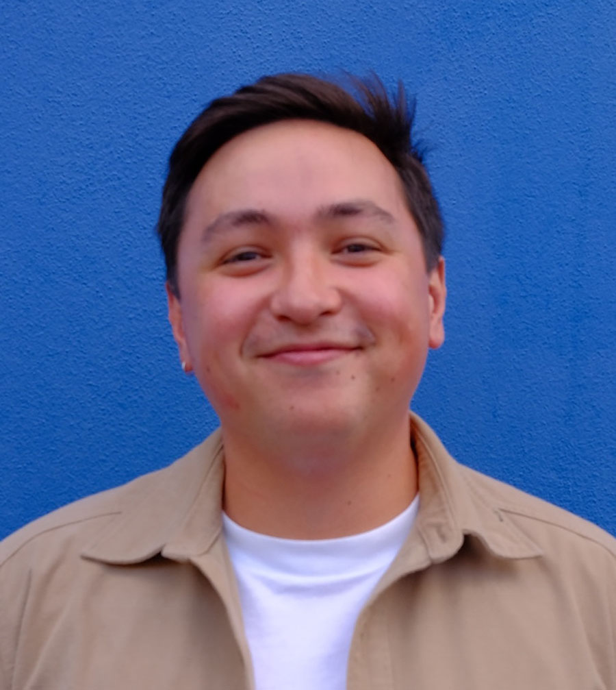 Grant Torre smiling in front of a bright blue wall, wearing a beige jacket over a white shirt.