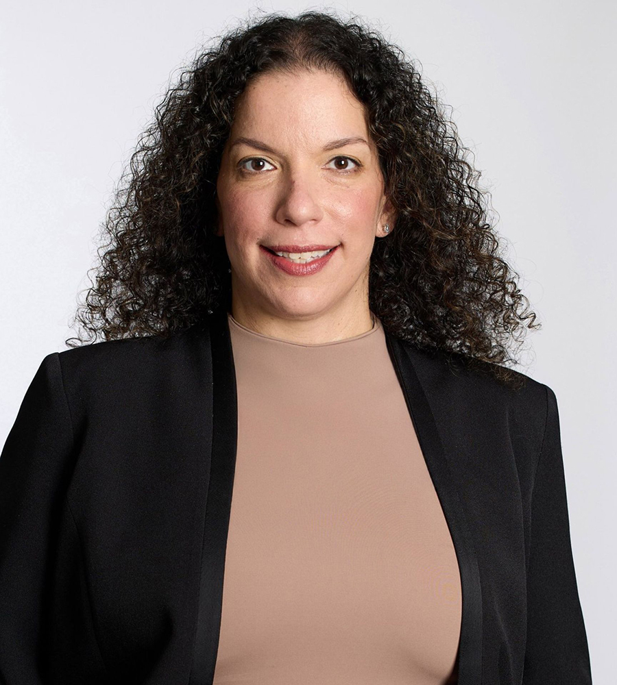 Hannah Shaul Bar Nissim with curly dark hair wearing a black blazer and beige top poses against a light background for a portrait used in the Geena Davis Institute’s event on disability representation in television.