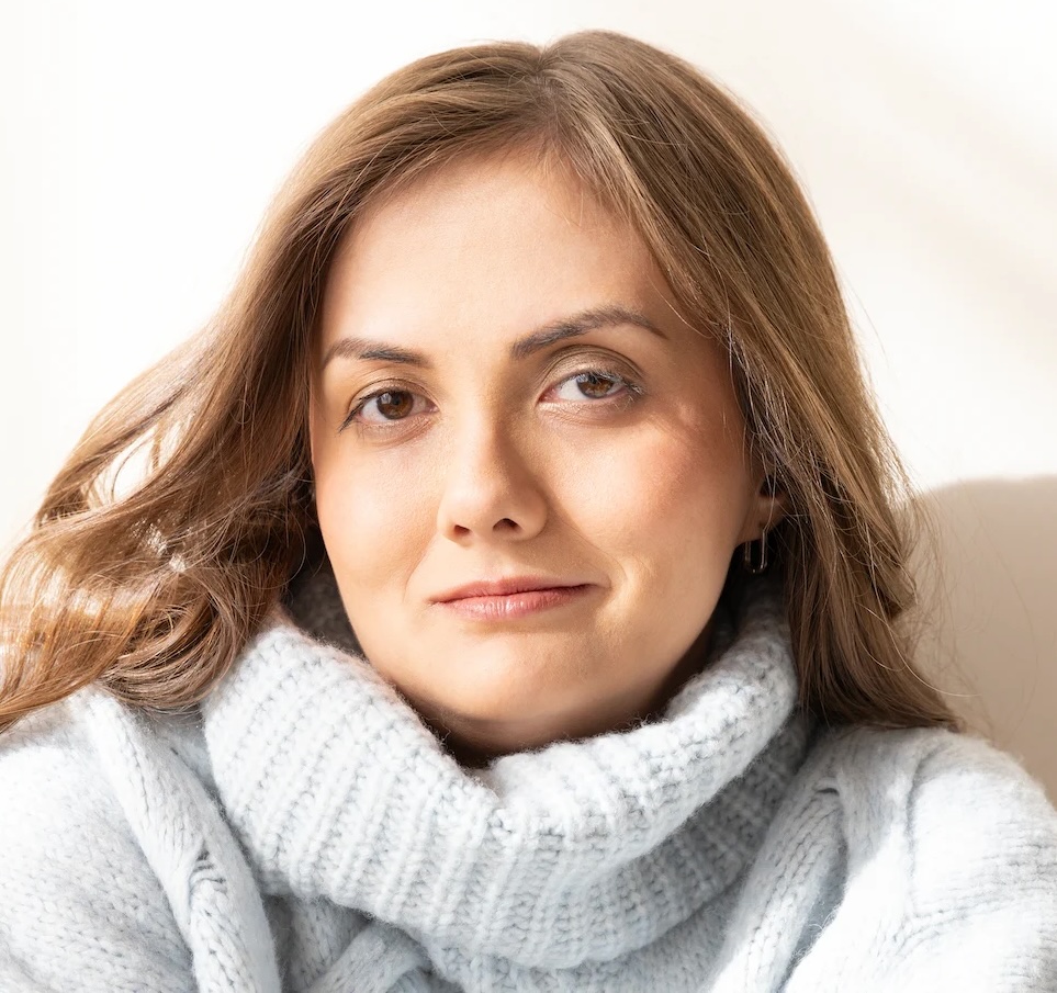 A close-up headshot portrait of actor Tal Anderson with light brown hair wearing a high-collared, light blue knit turtleneck sweater.
